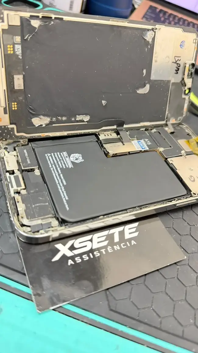 iPhone aberto na bancada mostrando a bateria, com o cartão da XSETE ao lado