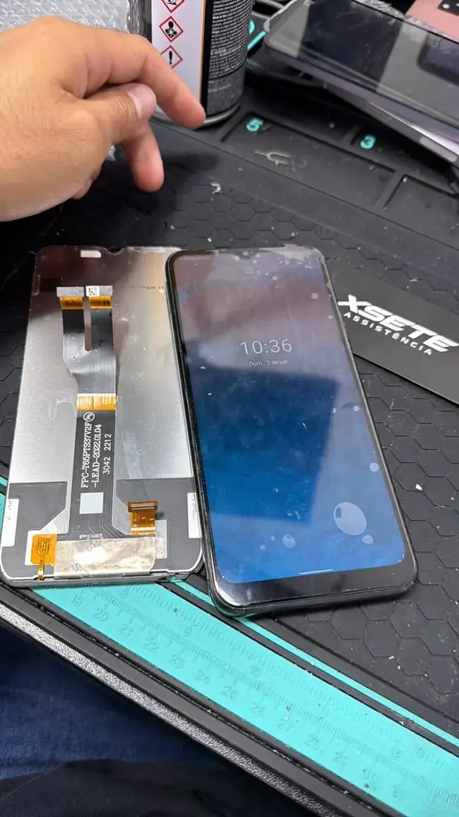 Tela nova com flat, ao lado do celular Android que será consertado, sobre uma bancada com o cartão da XSETE
