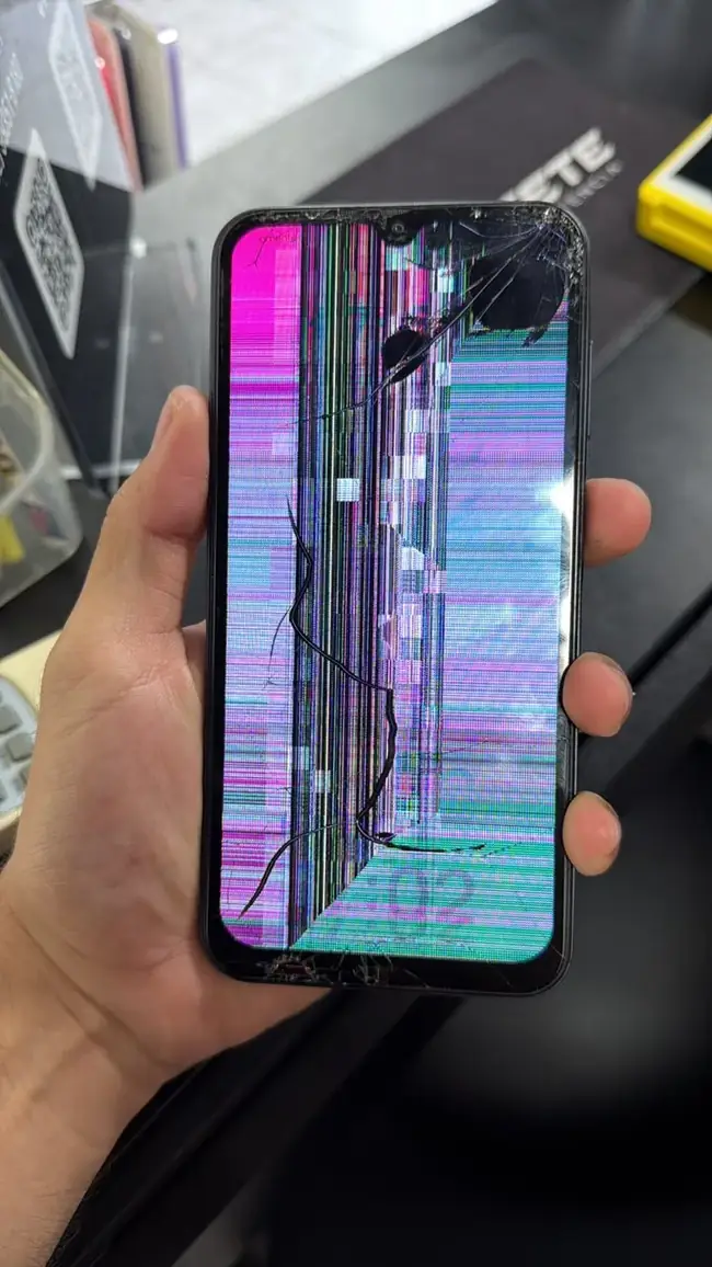 Celular Android com a tela trincada e listras coloridas, segurado na mão